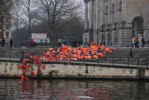 Installation aus Schwimmwesten Geflüchteter vor dem Reichstag in Berlin:<br>Mit einer Kunstinstallation aus mehreren Hundert Schwimmwesten am Spreebogen vor dem Reichstagsgebäude in Berlin hat die Seenotrettungsorganisation Sea-Watch am 5. Dezember zusammen mit dem Kollektiv ohne Namen auf das anhaltende Leid der Geflüchteten an den Außengrenzen der EU aufmerksam gemacht.<br>Die Aktion sei „ein Appell an die neue Bundesregierung, Migration und Flucht zu entkriminalisieren, sichere Fluchtwege nach Deutschland und Europa zu schaffen und das Sterben im Mittelmeer zu stoppen“, heißt es in einer Stellungnahme der beiden Initiatoren. Das organisierte Elend an den EU-Außengrenzen sei menschengemacht und gewollt, es fehle der politische Wille zur Veränderung. „Die neue Bundesregierung unter Olaf Scholz muss sofort handeln, sonst macht sie sich mitschuldig“, so Oliver Kulikowski von Sea-Watch.<br>Die Schwimmwesten wurden vom sogenannten „Westenfriedhof“ auf der griechischen Insel Lesbos eingesammelt und nach Berlin gebracht. Menschen, die im Camp Kara Tepe auf Lesbos leben, haben die Schwimmwesten mit Botschaften an die Entscheidungsträger in Deutschland und Europa beschriftet.<br>https://sea-watch.org/